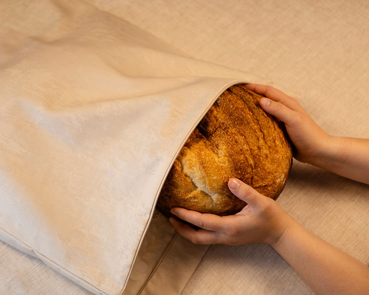 Artisan loaf being placed inside the Linen & Loaf challah cover bread storage compartment